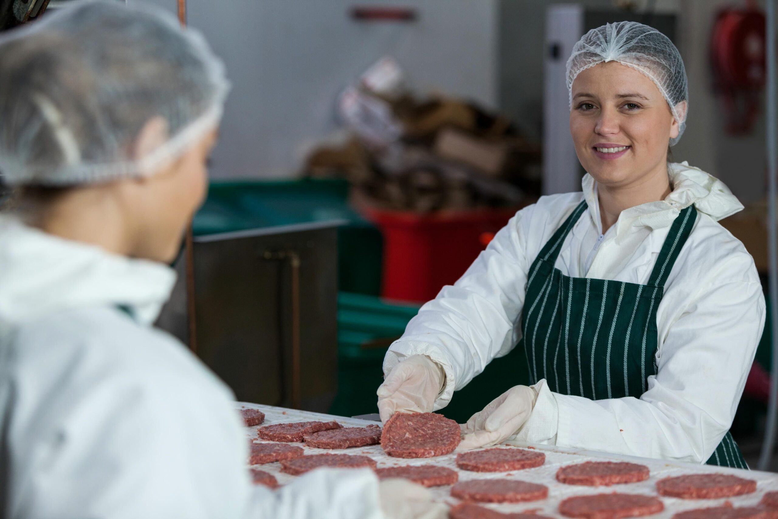 Female butchers processing hamburger patty at meat factory